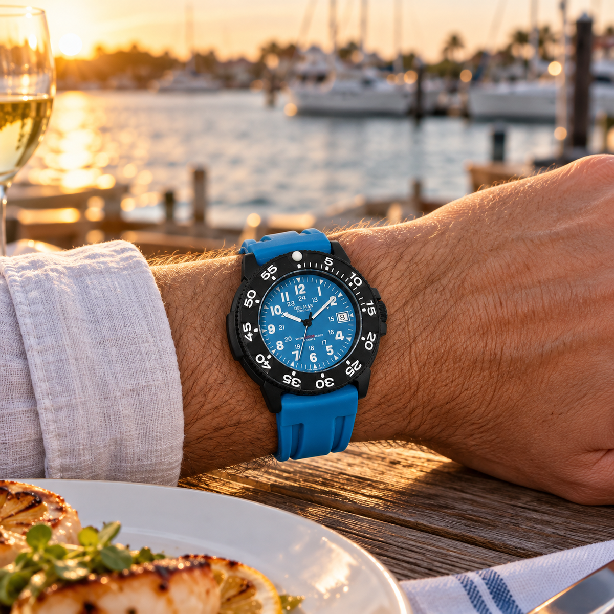 Del Mar Sand Key 50387 watch with a blue dial and matching blue sport strap, worn at a waterfront dinner at sunset.